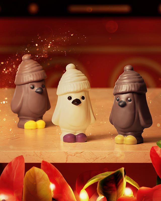 Three chocolate figurines, resembling birds in hats, on a festive background
