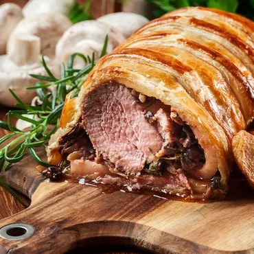 Sliced beef Wellington on a wooden board with mushrooms and rosemary