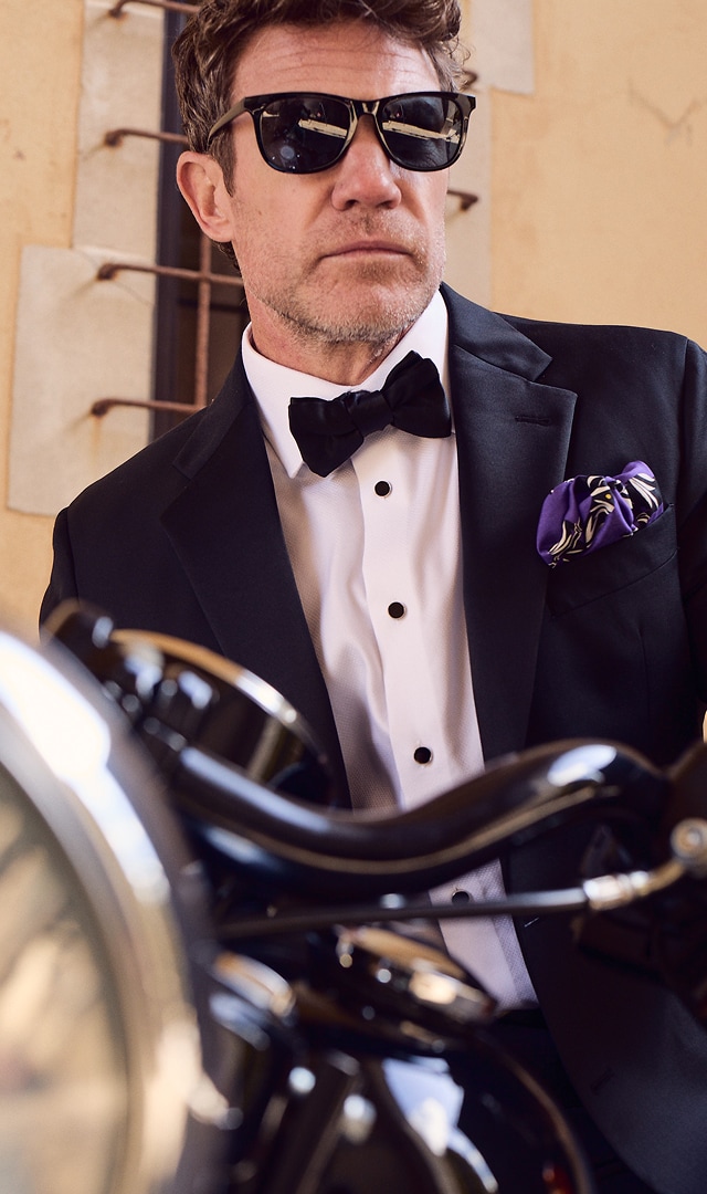 Man in tuxedo and sunglasses standing beside a motorcycle