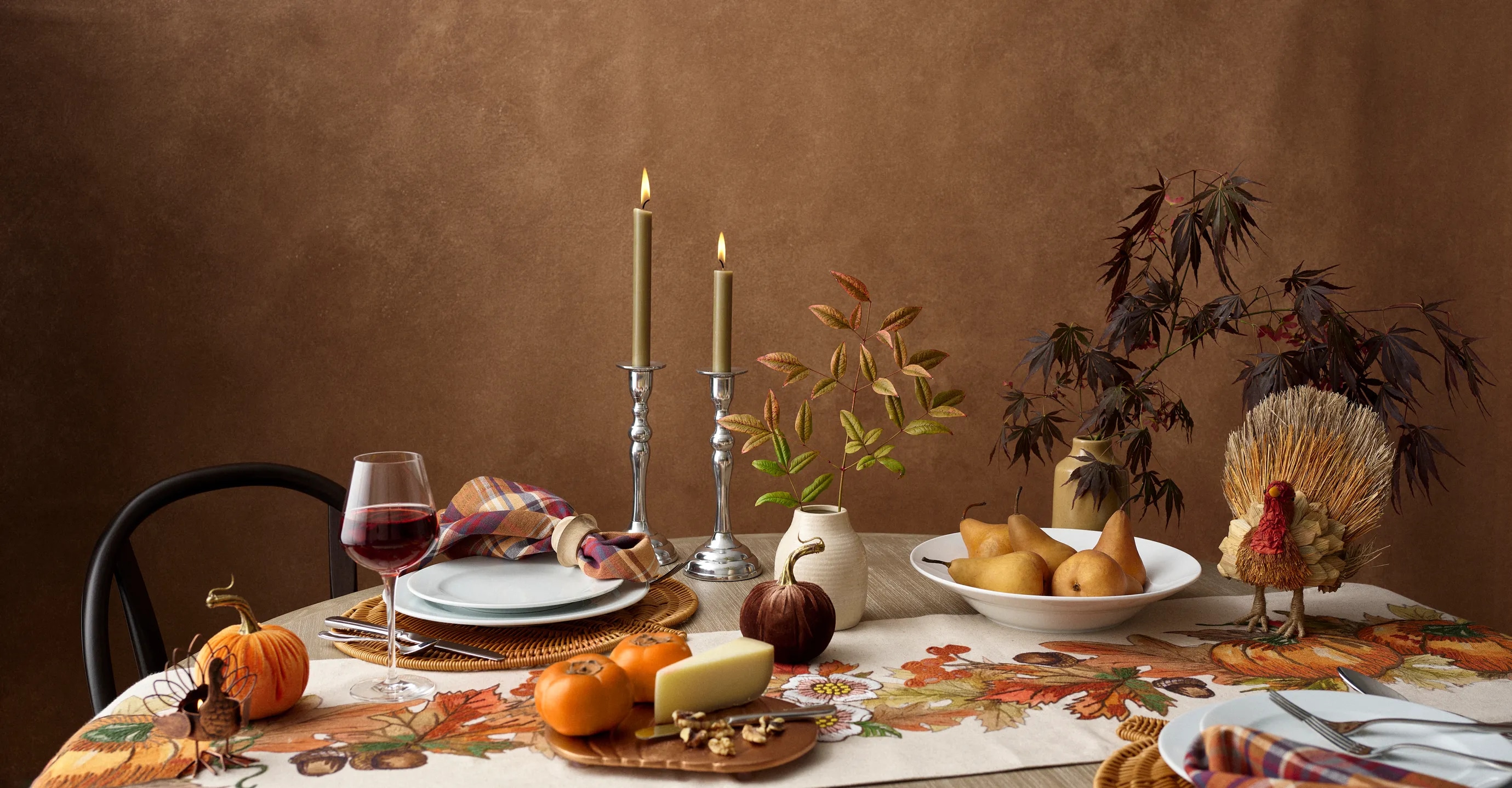 Elegant autumn-themed dining table setup with candles, wine, and seasonal decorations