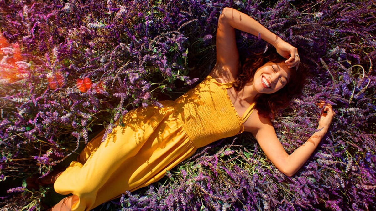 Woman in yellow dress lying in colorful flowers, smiling with hand on her head