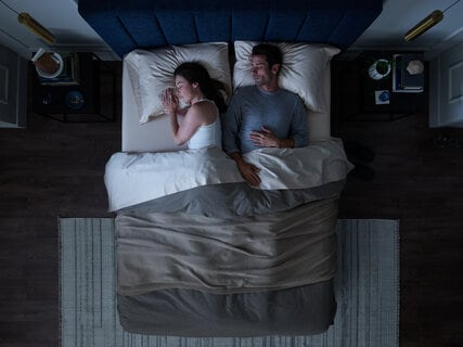 Overhead view of a couple in bed, woman reading and man using a tablet, in a dark room