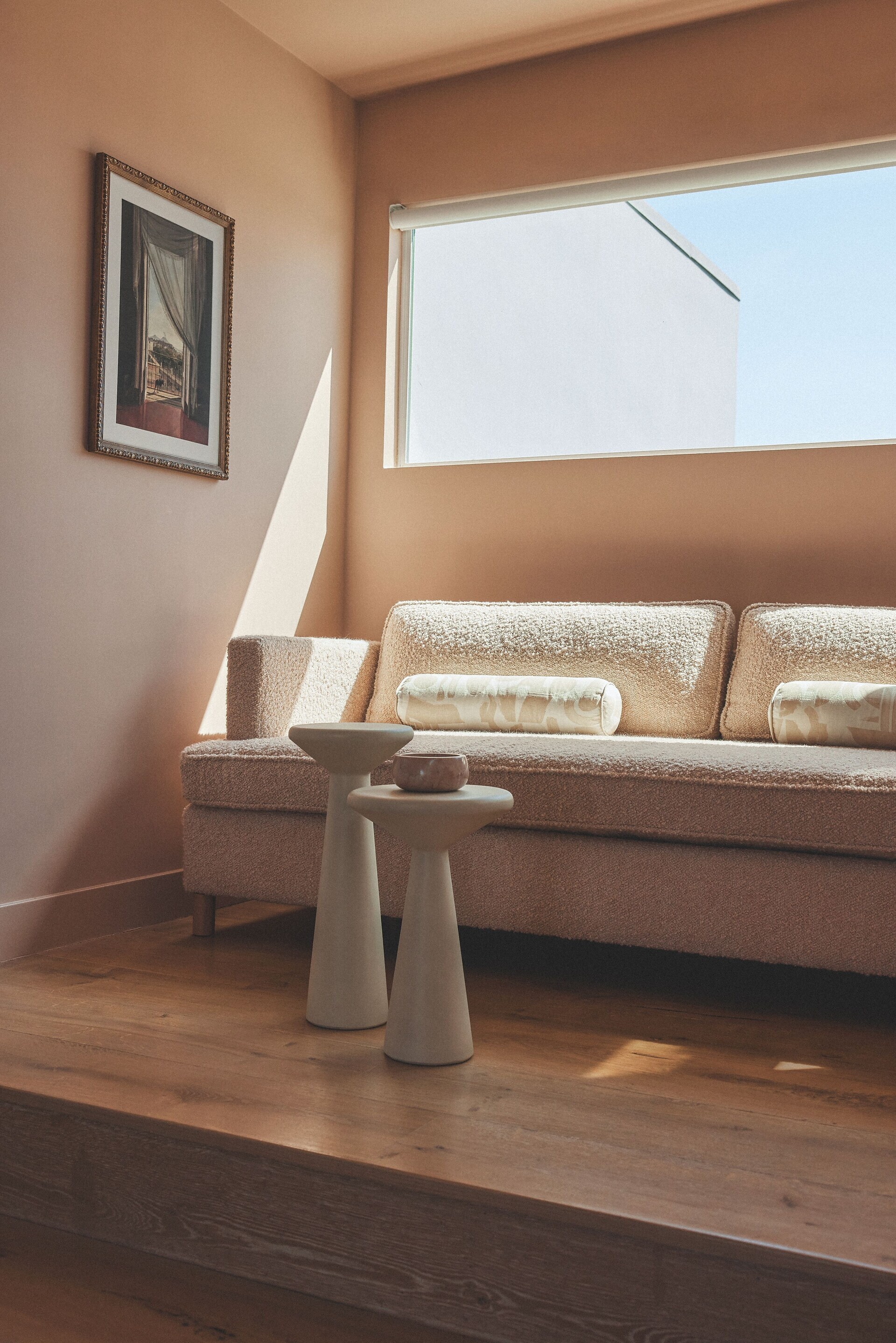 Cozy living room with a large couch under a window, decorative vases on the floor, and framed art on the wall