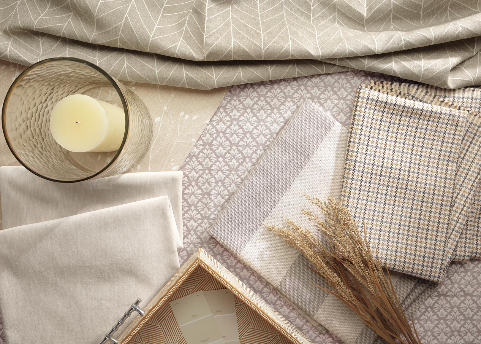 Neutral-toned bedding, notebooks, dried grass, and a candle on a cozy bed setup