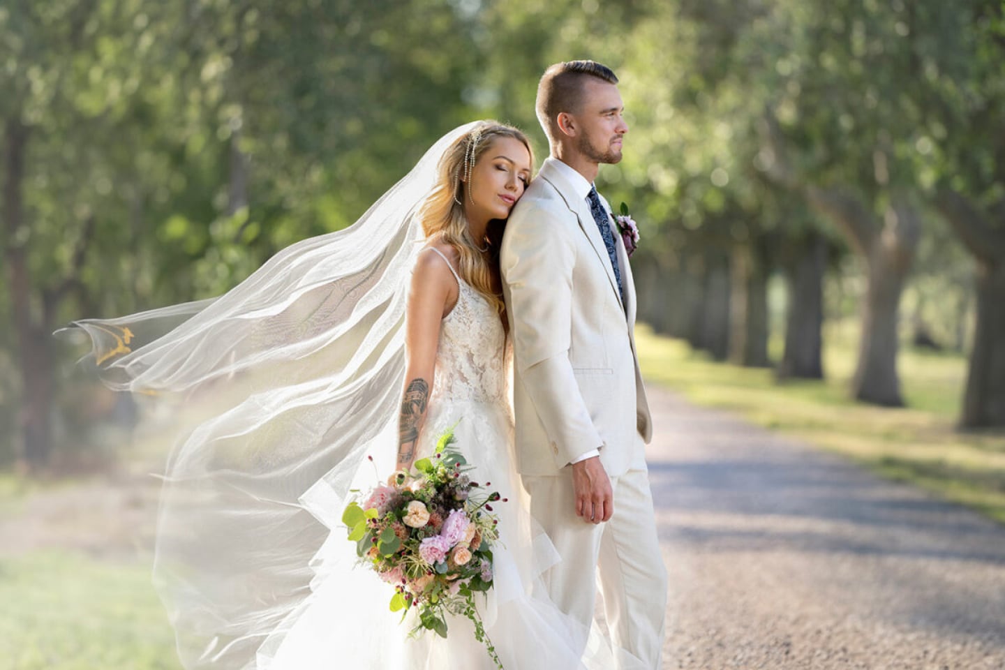 Bride and groom walking under trees, bride holding bouquet