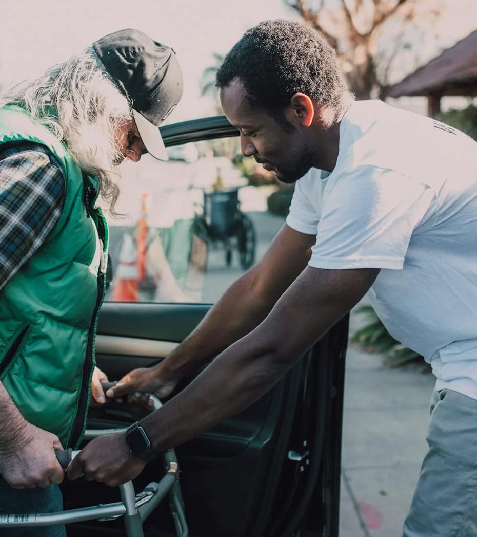 Young man assisting elderly person with walker into a car