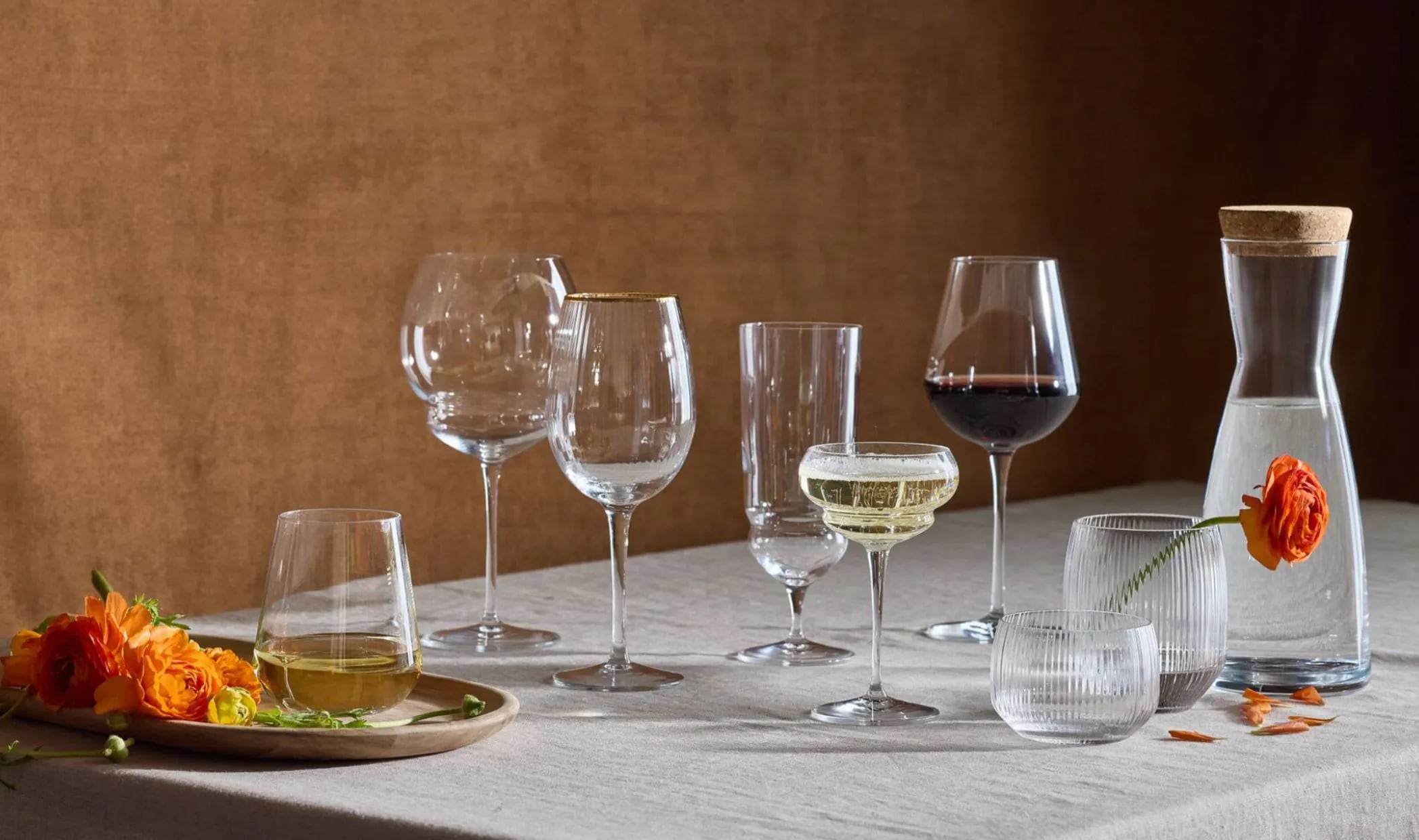 Elegant dining table setup with various empty and filled wine glasses, a carafe of wine, and a plate with autumn leaves