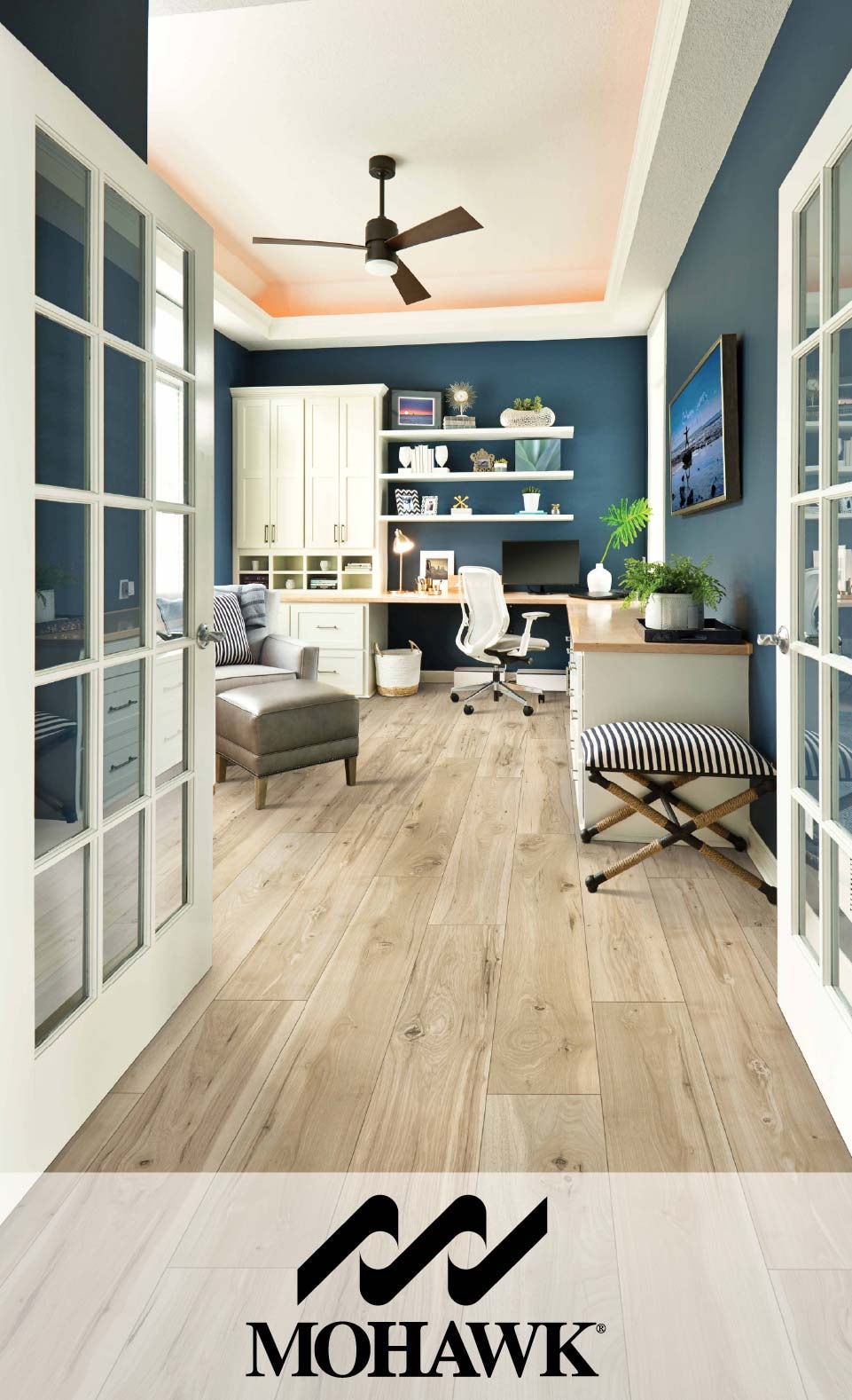 Elegant home office with blue walls, wooden flooring, and stylish furniture, featuring a logo of Mohawk at the bottom
