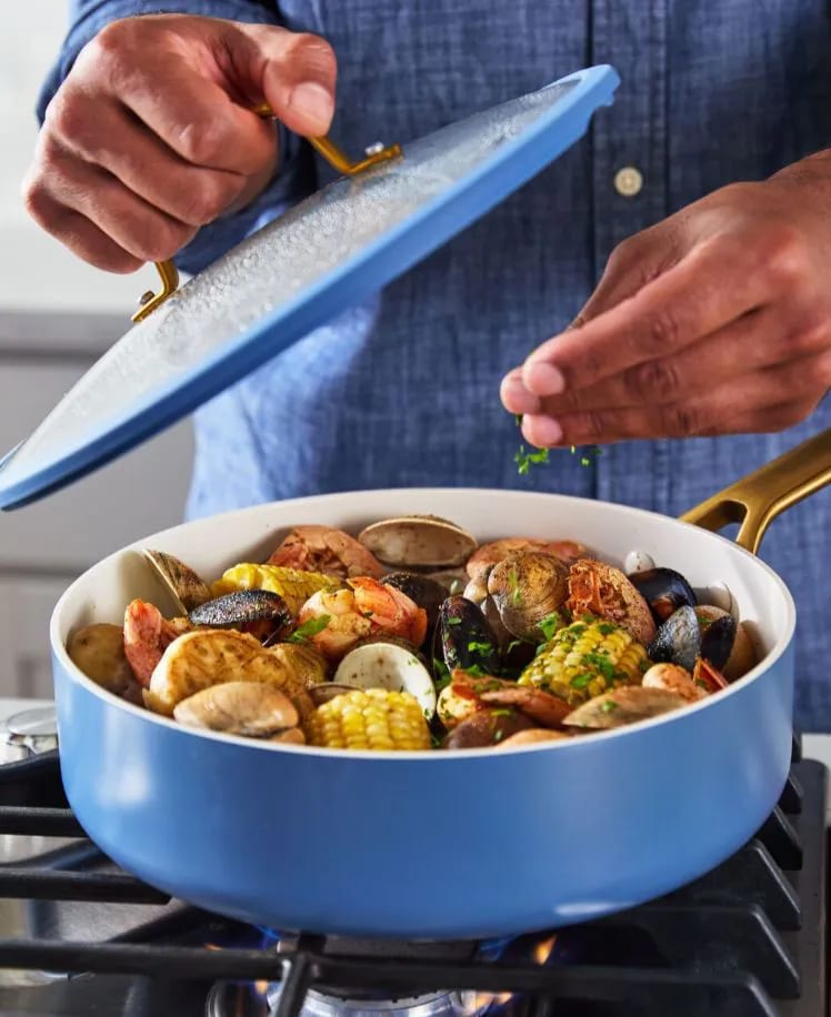 Man garnishing a pot of seafood and vegetables on a stove