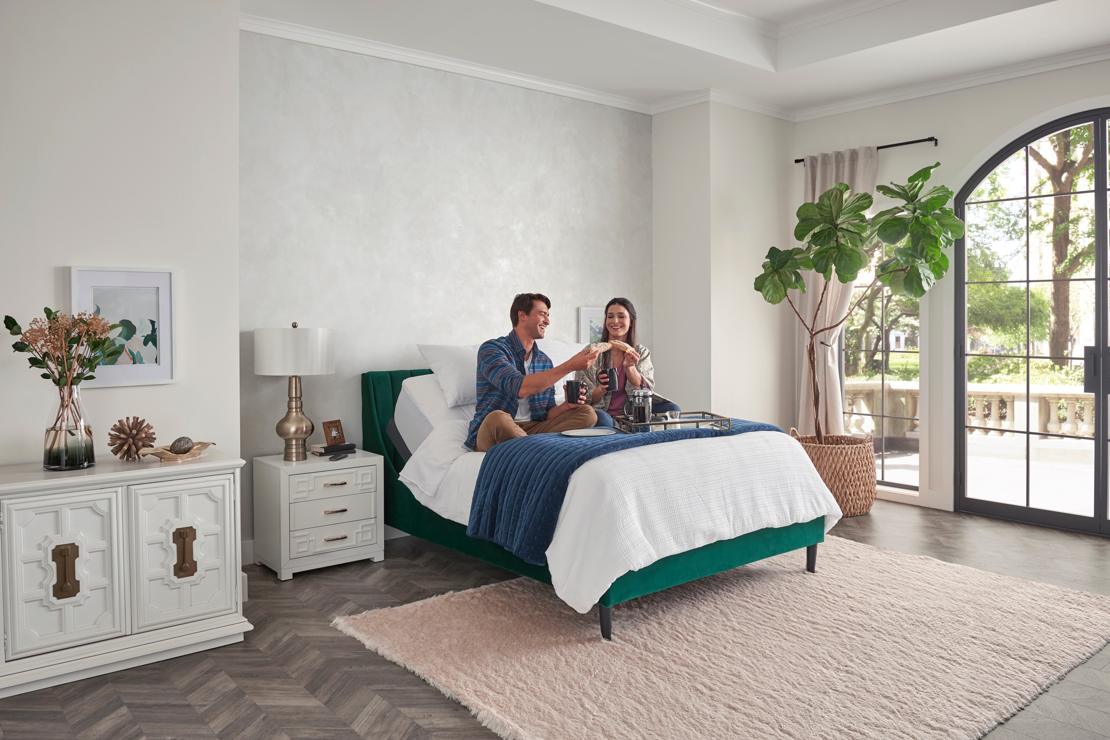 Couple and dog sitting on bed in a bright, stylish bedroom