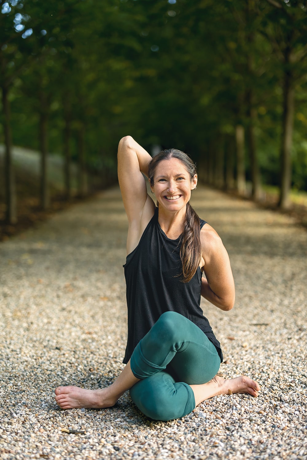 Femme souriante pratiquant le yoga dans un parc, en tenue de sport noire et verte