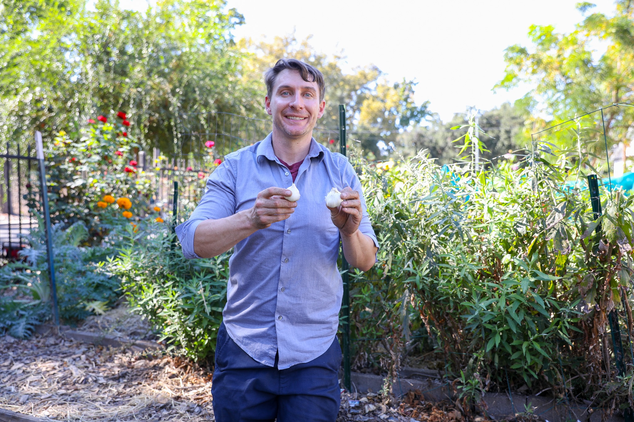 Man smiling, holding two ice cream cones in a garden
