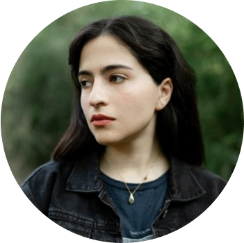 Young woman with dark hair in a denim jacket looking away contemplatively outdoors