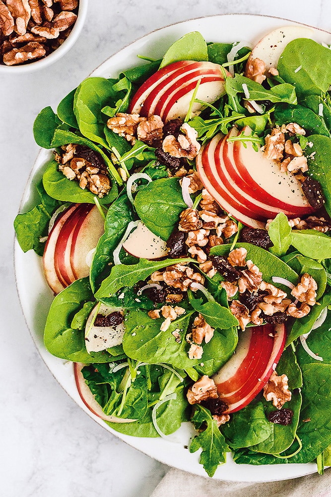 Fresh spinach salad with apple slices, walnuts, and a balsamic dressing on a white plate