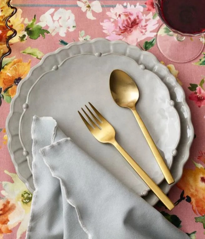 Gold fork and spoon on a plate with a floral tablecloth and gray napkin