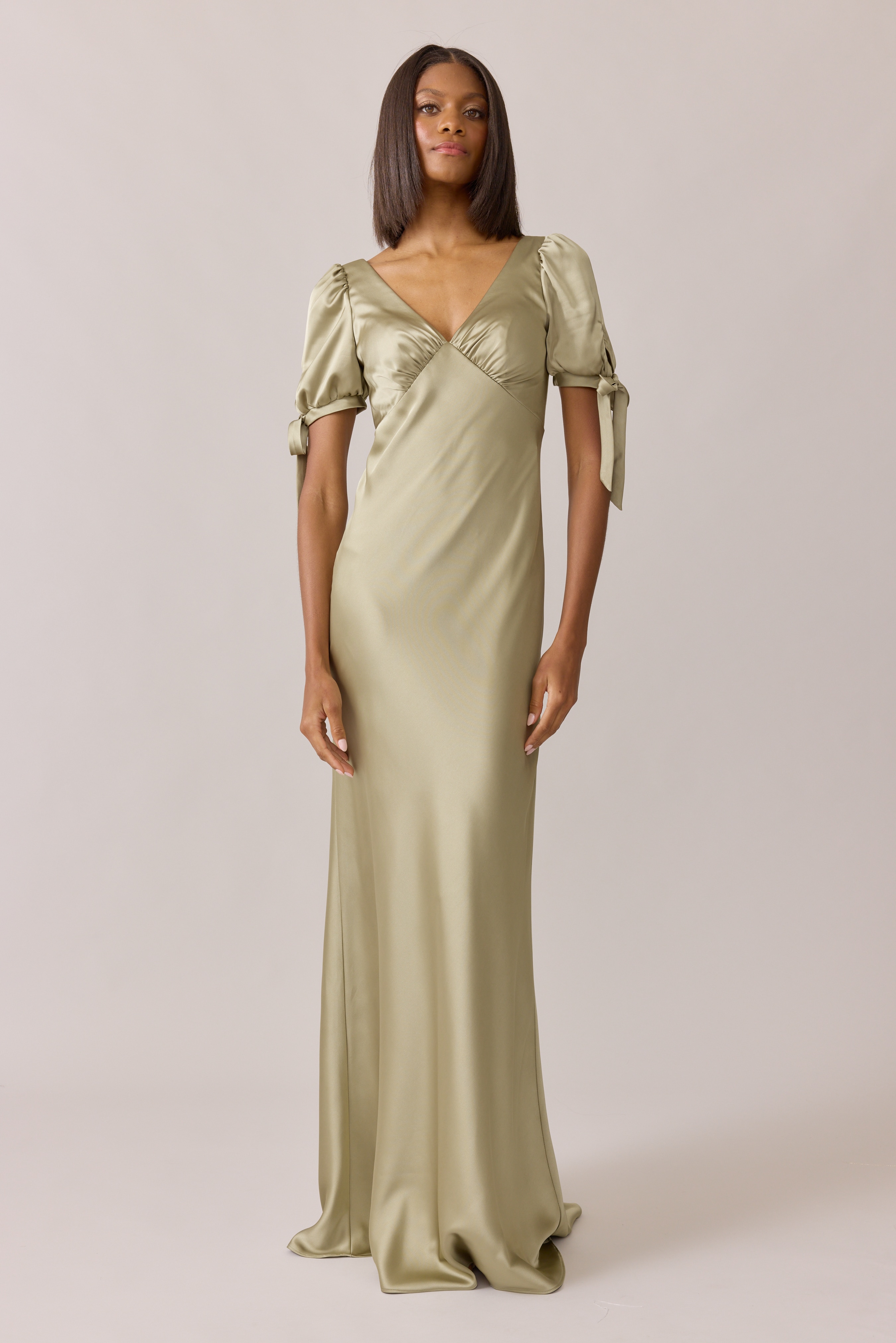 Woman in elegant, long, pastel green dress standing against a plain background