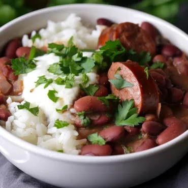 Bowl of red beans with sausage slices, topped with sour cream and cilantro on rice