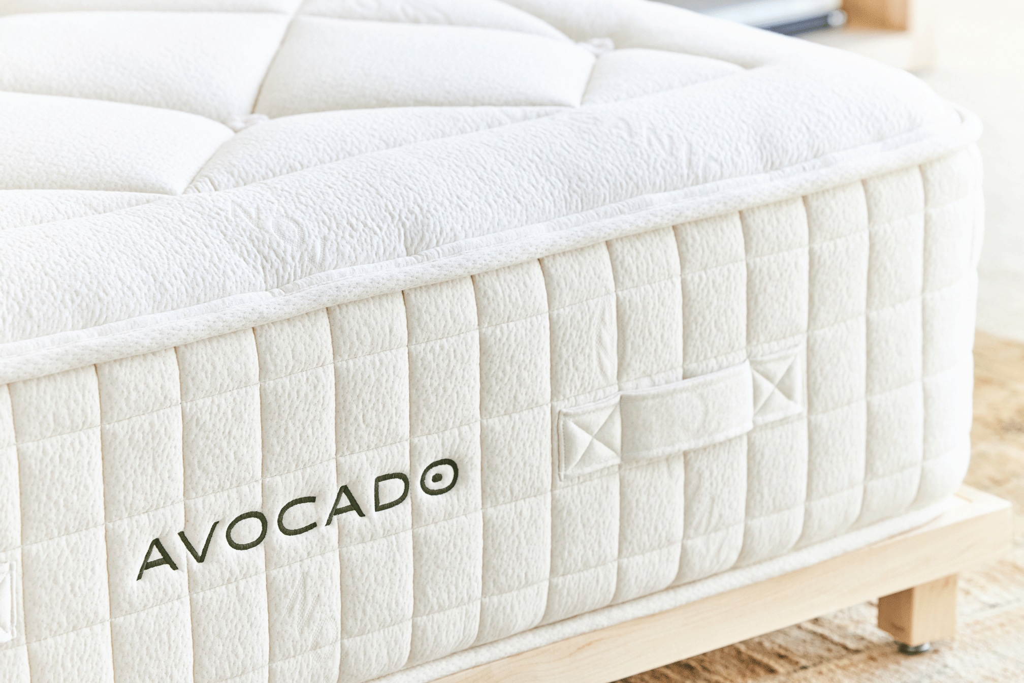 Close-up of a white Avocado brand mattress on a wooden bed frame