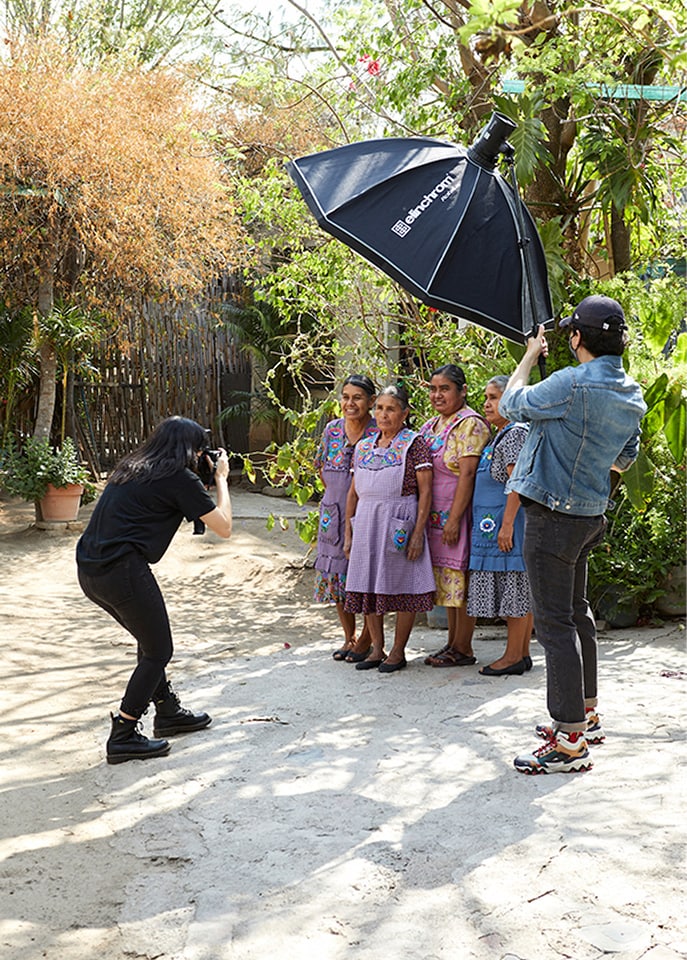Photographer taking a picture of four women while an assistant holds a light umbrella in a garden