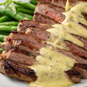 Sliced steak with béarnaise sauce and green beans on the side