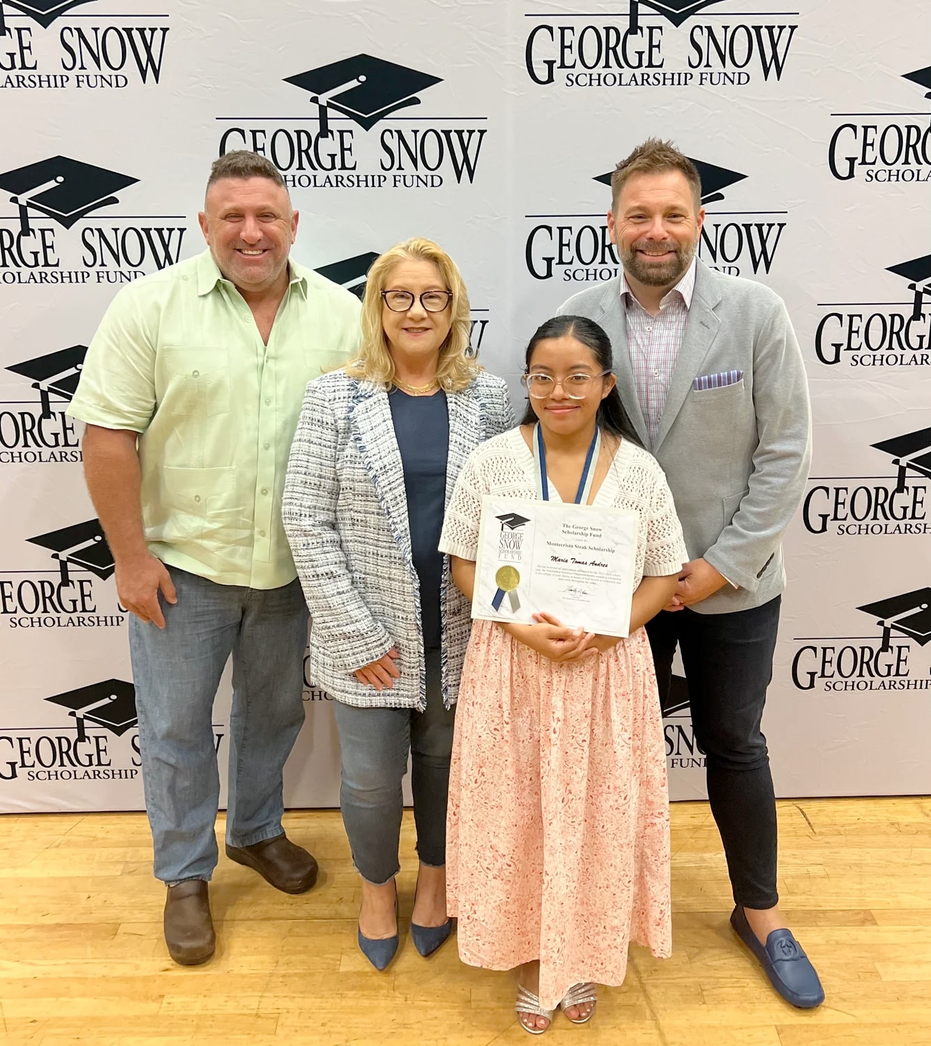 Four people posing at event, young girl holding a certificate, backdrop with "George Snow" logos