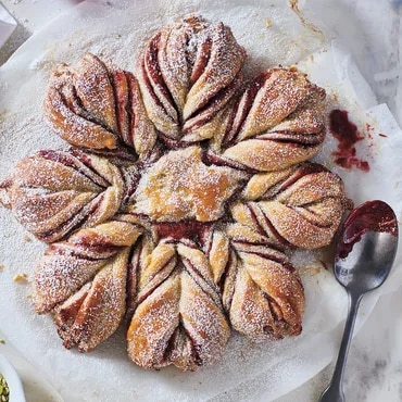 Star-shaped pastry with powdered sugar and fruit filling, served on a table with a spoon