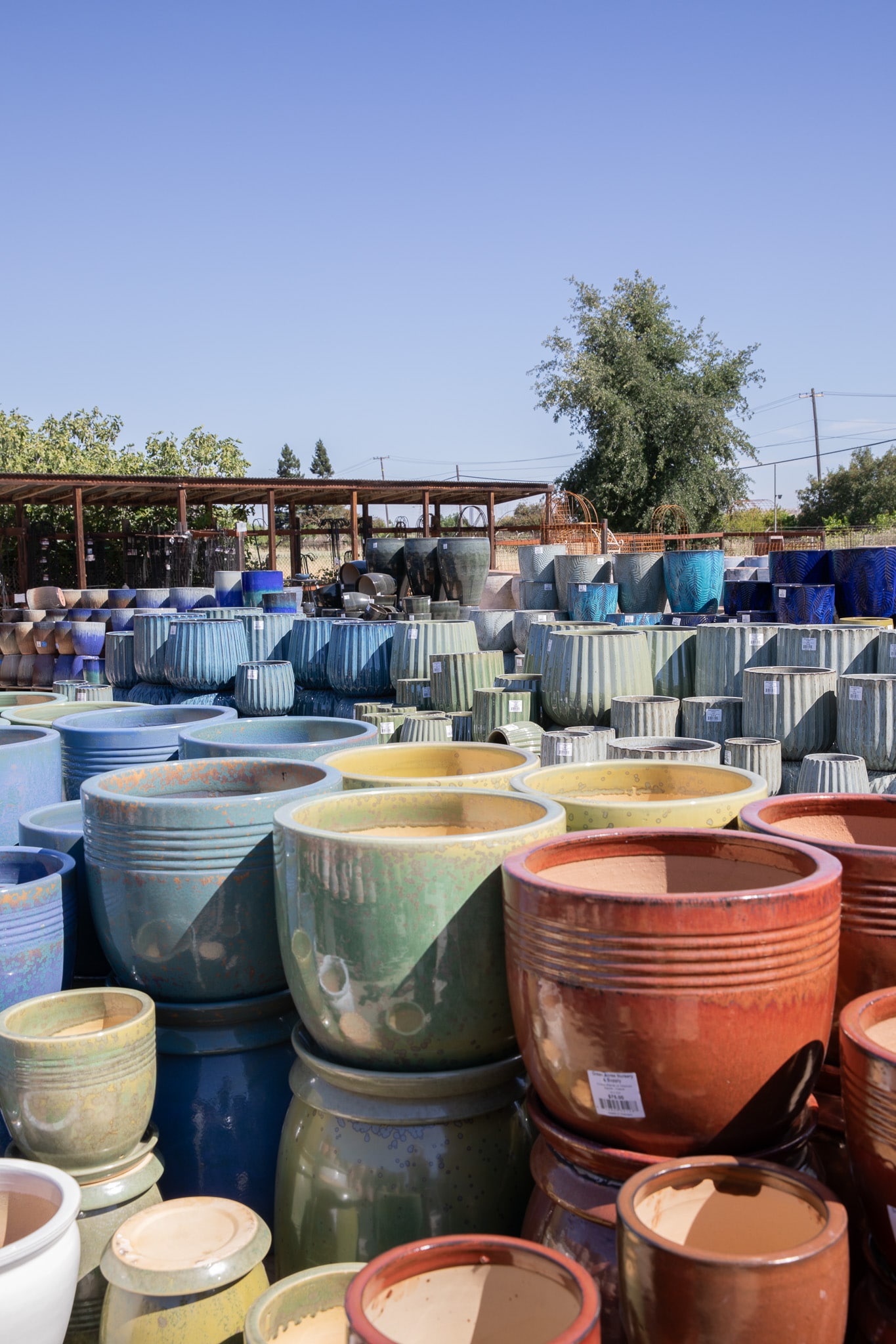 Outdoor pottery store displaying colorful ceramic pots in various sizes under clear skies