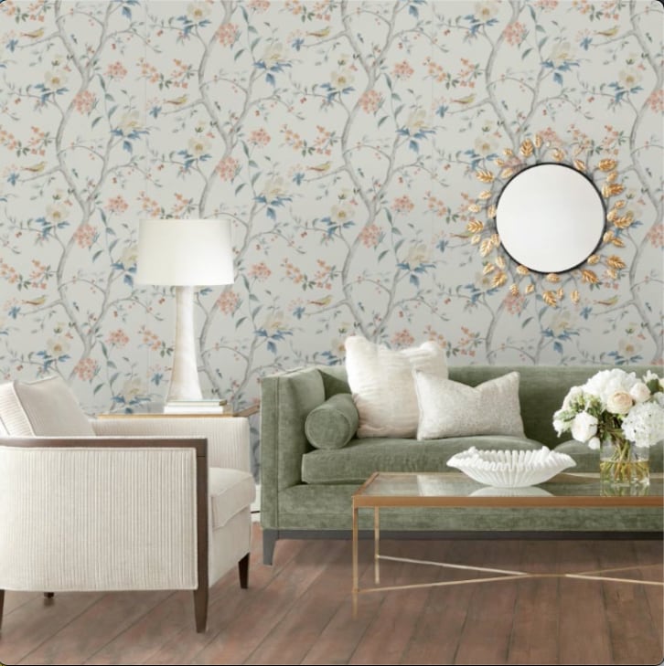 Elegant living room with floral wallpaper, green sofa, white chairs, and a round mirror