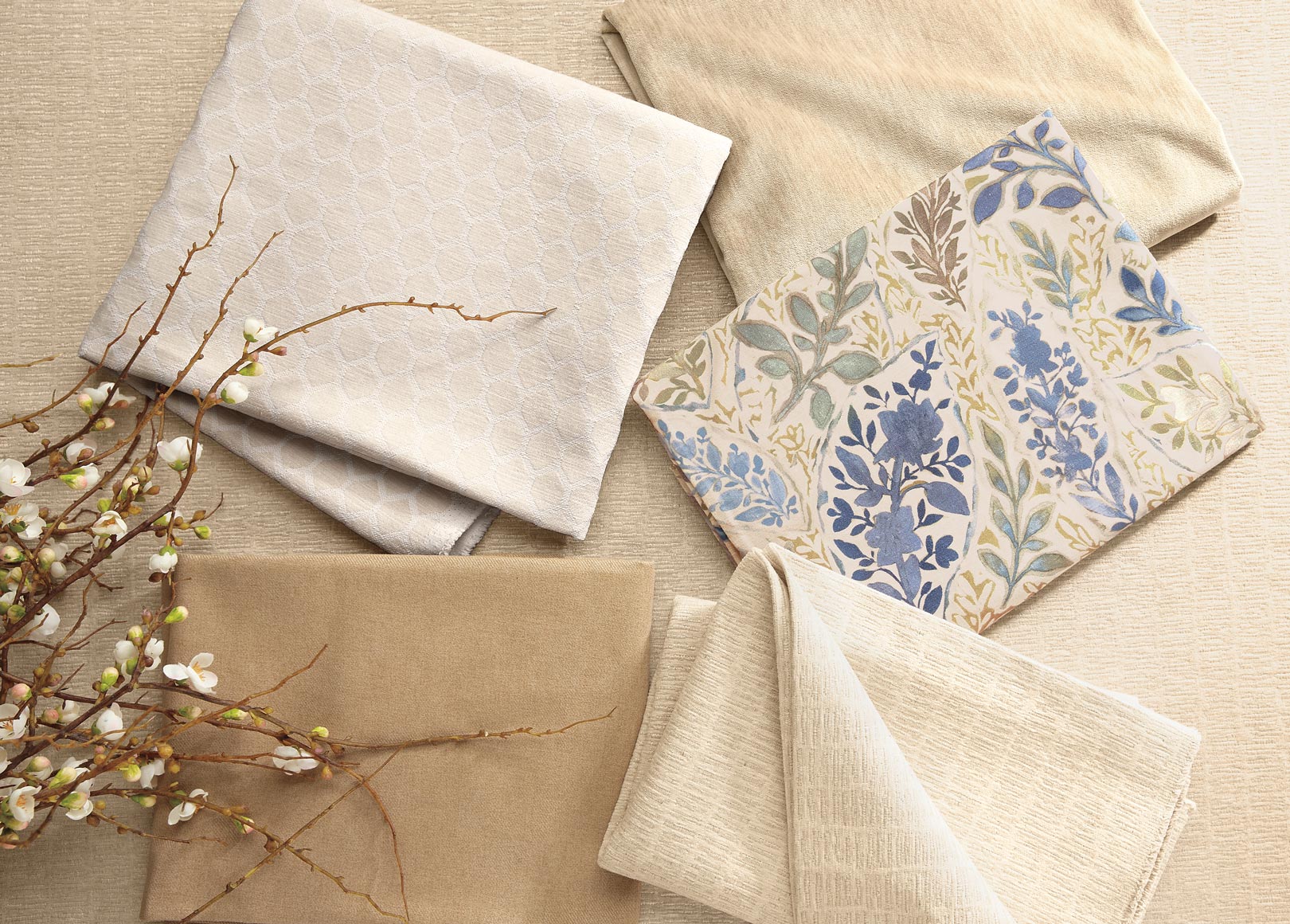 Assorted fabric swatches with floral patterns alongside branches on a beige background