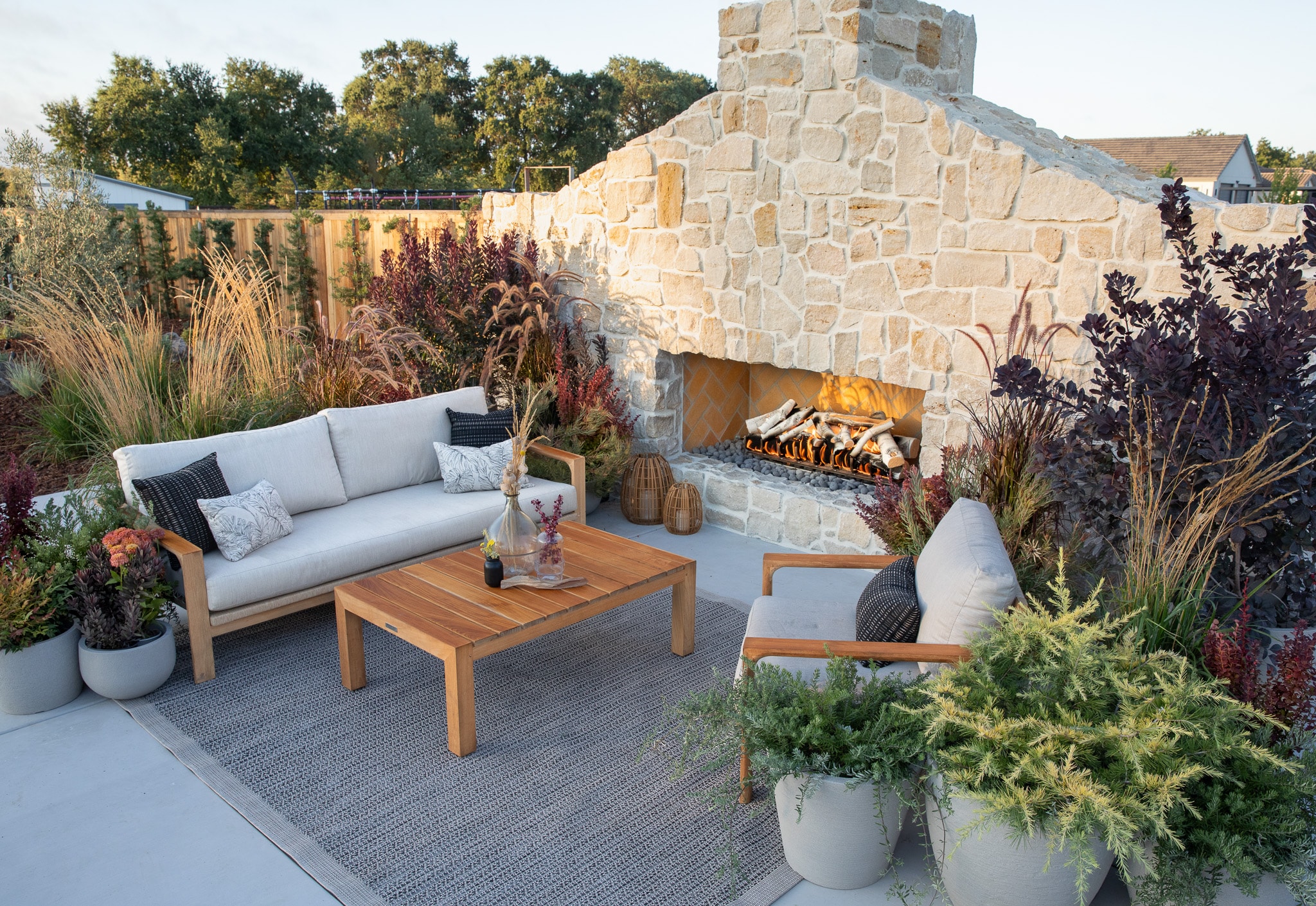 Outdoor patio with sofa, wooden table, and fireplace surrounded by plants