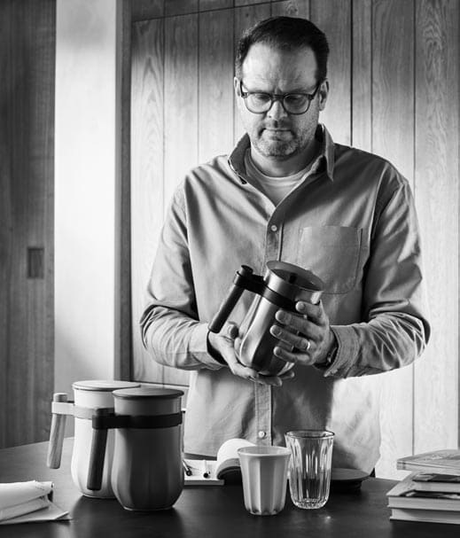 Man in glasses examines a blender in a kitchen with paperwork on the table
