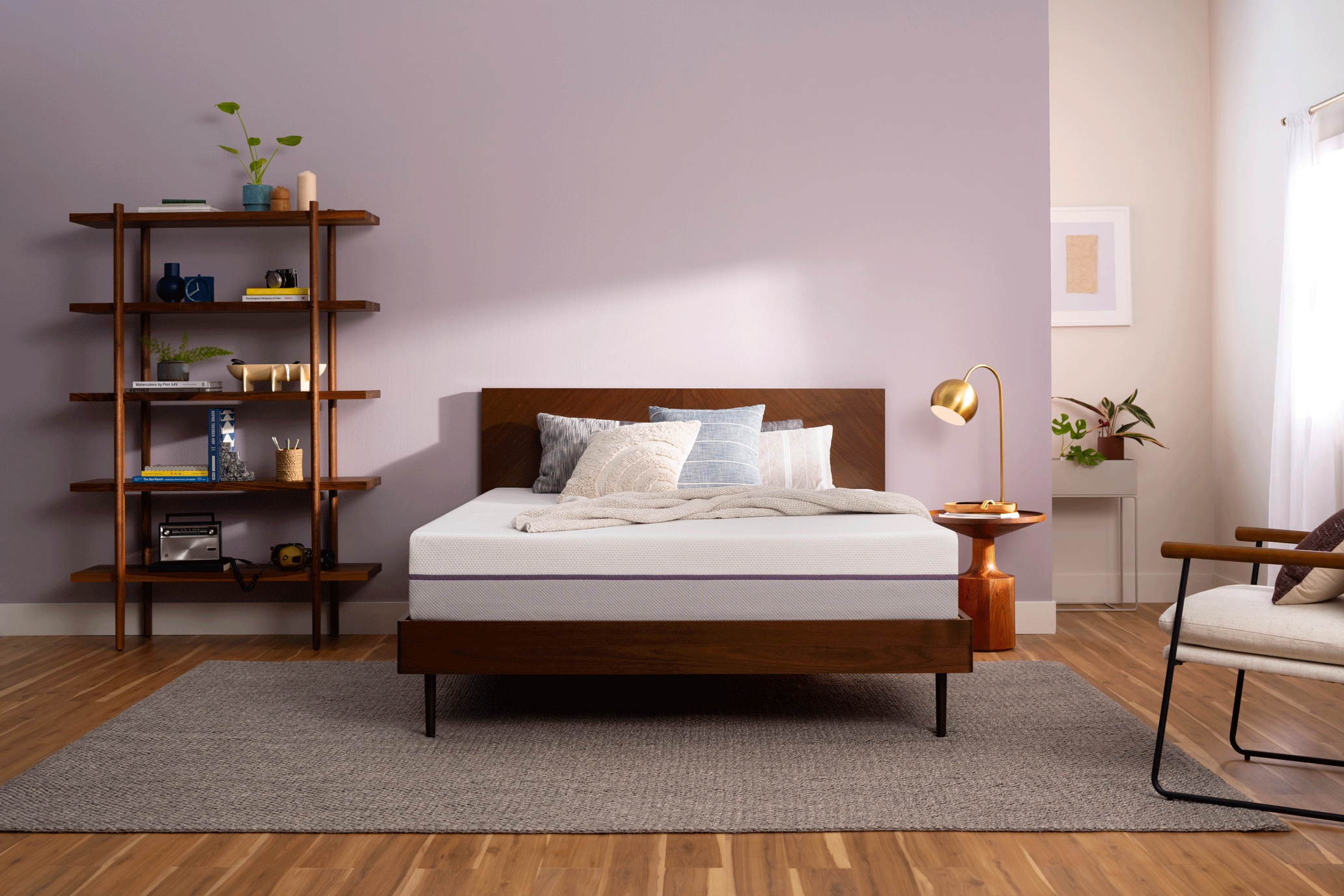 Modern bedroom with a wooden bed, side tables, chair, and shelving unit filled with decor