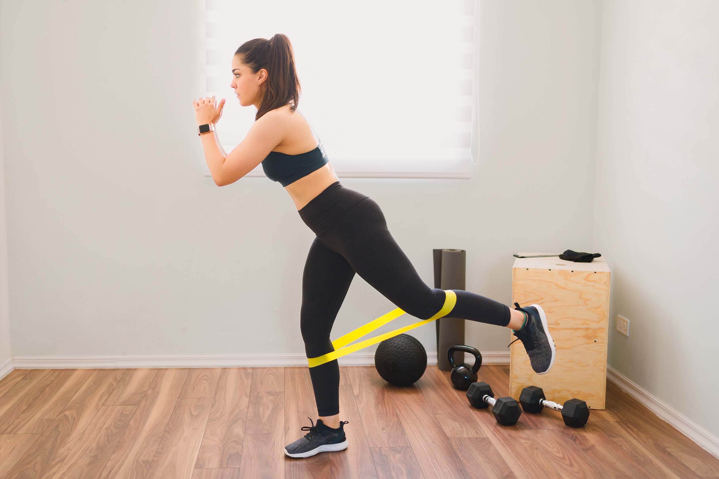 Femme s'exerçant avec une bande de résistance, vêtements de sport et haltères visibles