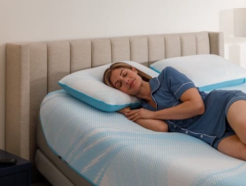 Woman sleeping peacefully on a bed with blue pillows in a bright bedroom
