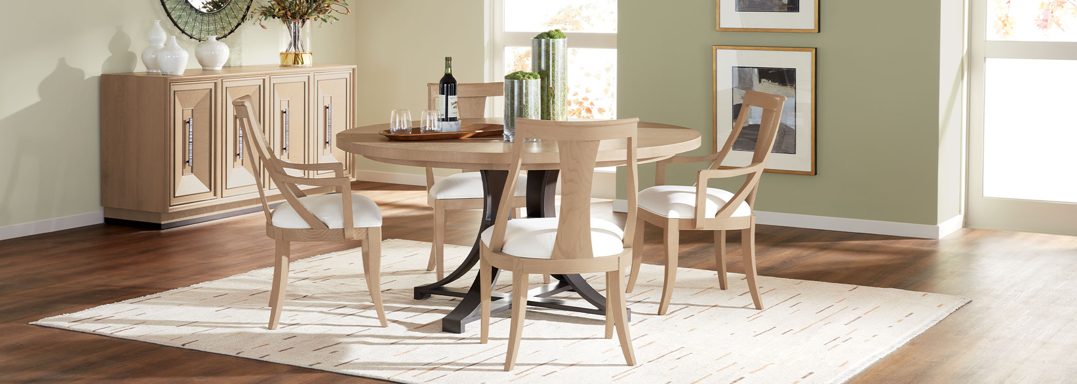 Round wooden dining table with four chairs in a bright room with wine and glasses