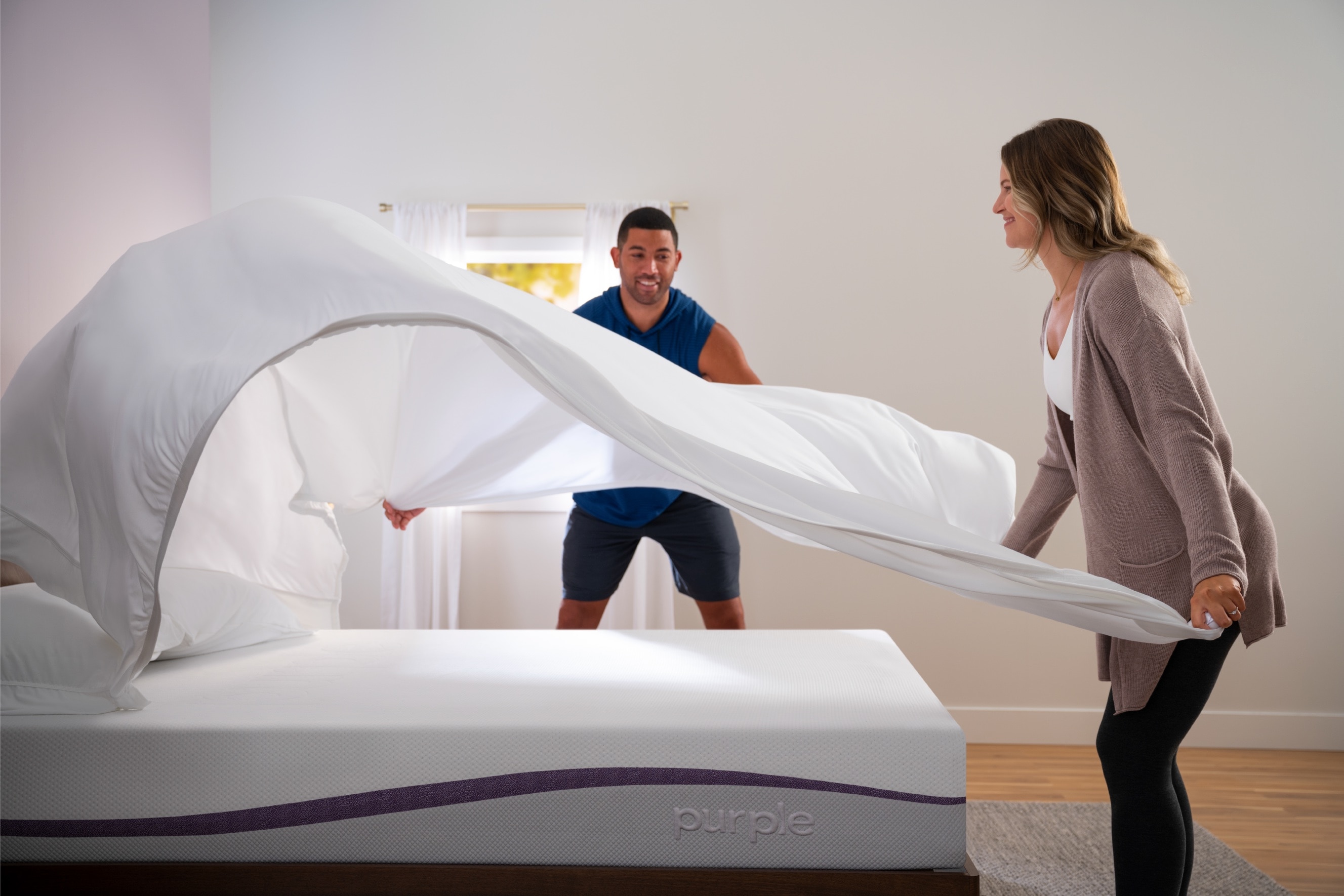 Man and woman making a bed, man flipping a white blanket in the air