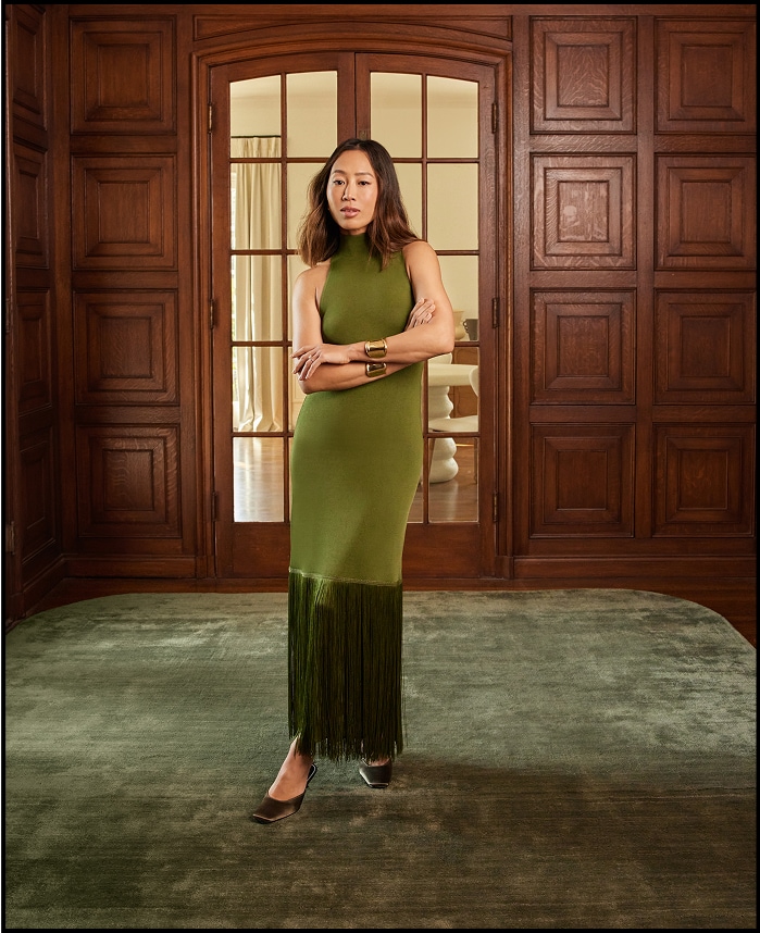 Woman in green dress standing in a room with wooden paneling