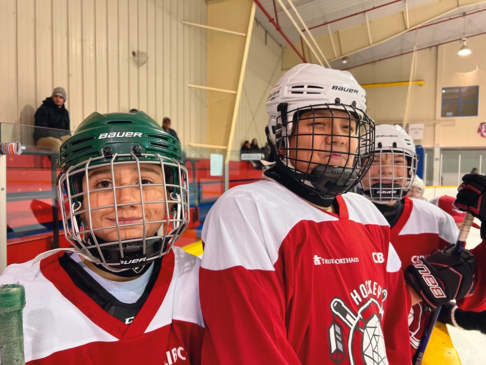 Trois jeunes joueurs de hockey en équipement, souriant sur la glace
