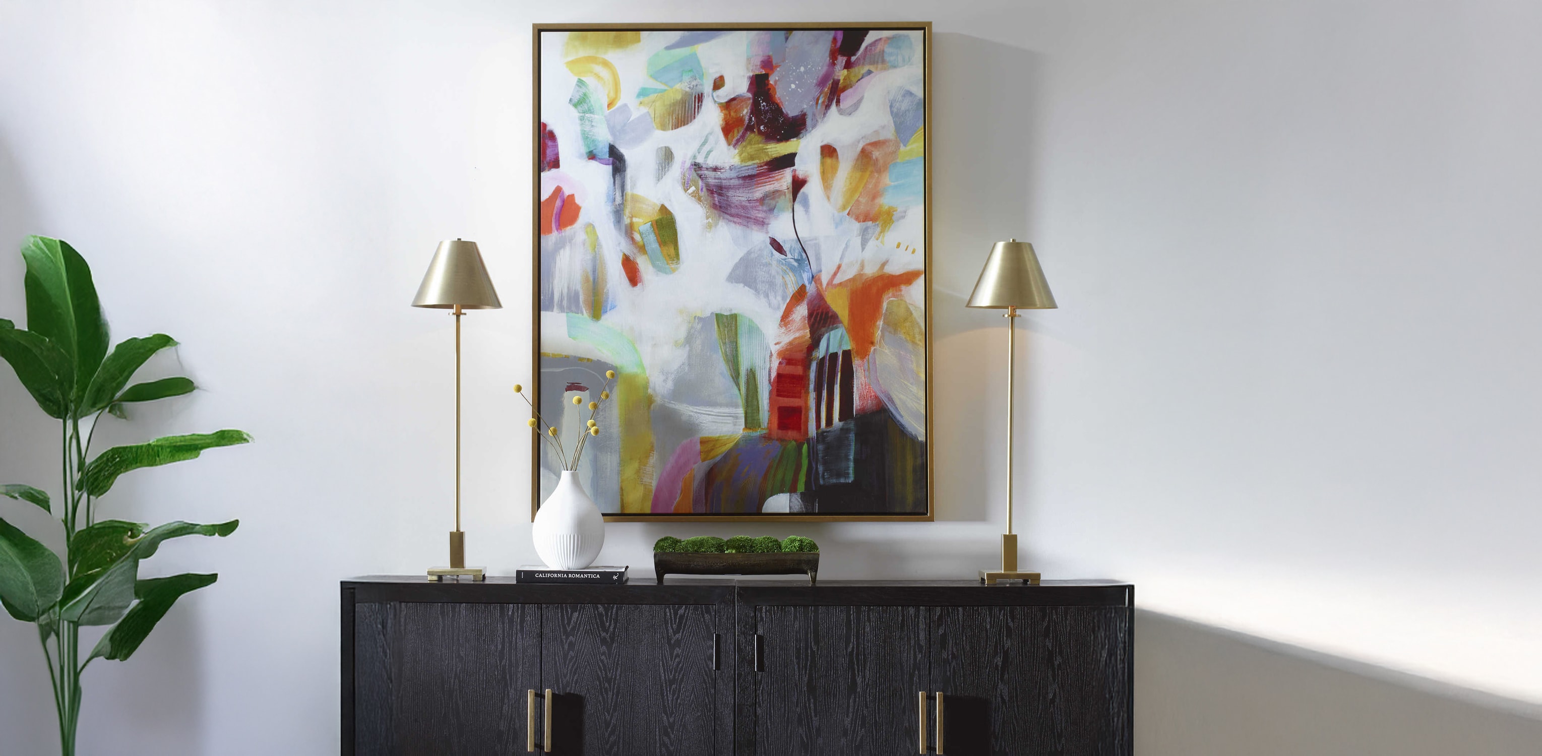 Modern living room with abstract painting, black cabinet, brass lamps, and a green plant