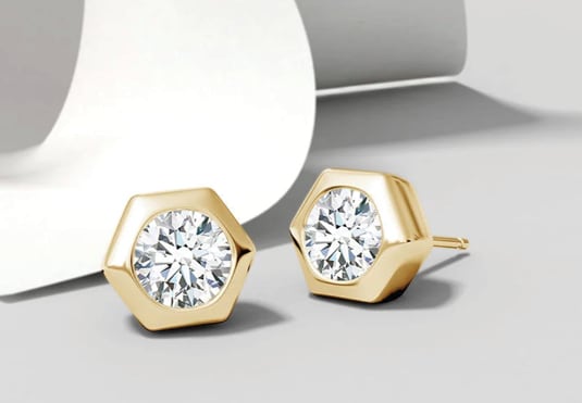 A pair of octagonal gold earrings with large diamonds, displayed on a gray surface