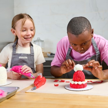 Two kids in aprons decorating cakes at a table