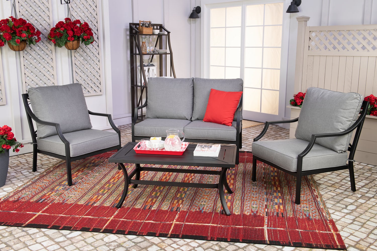 Patio furniture set with two chairs, a sofa, and a coffee table on a red rug, decorated with red pillows