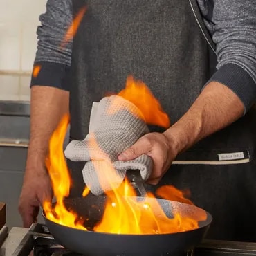 Person cooking with a flaming pan in a kitchen