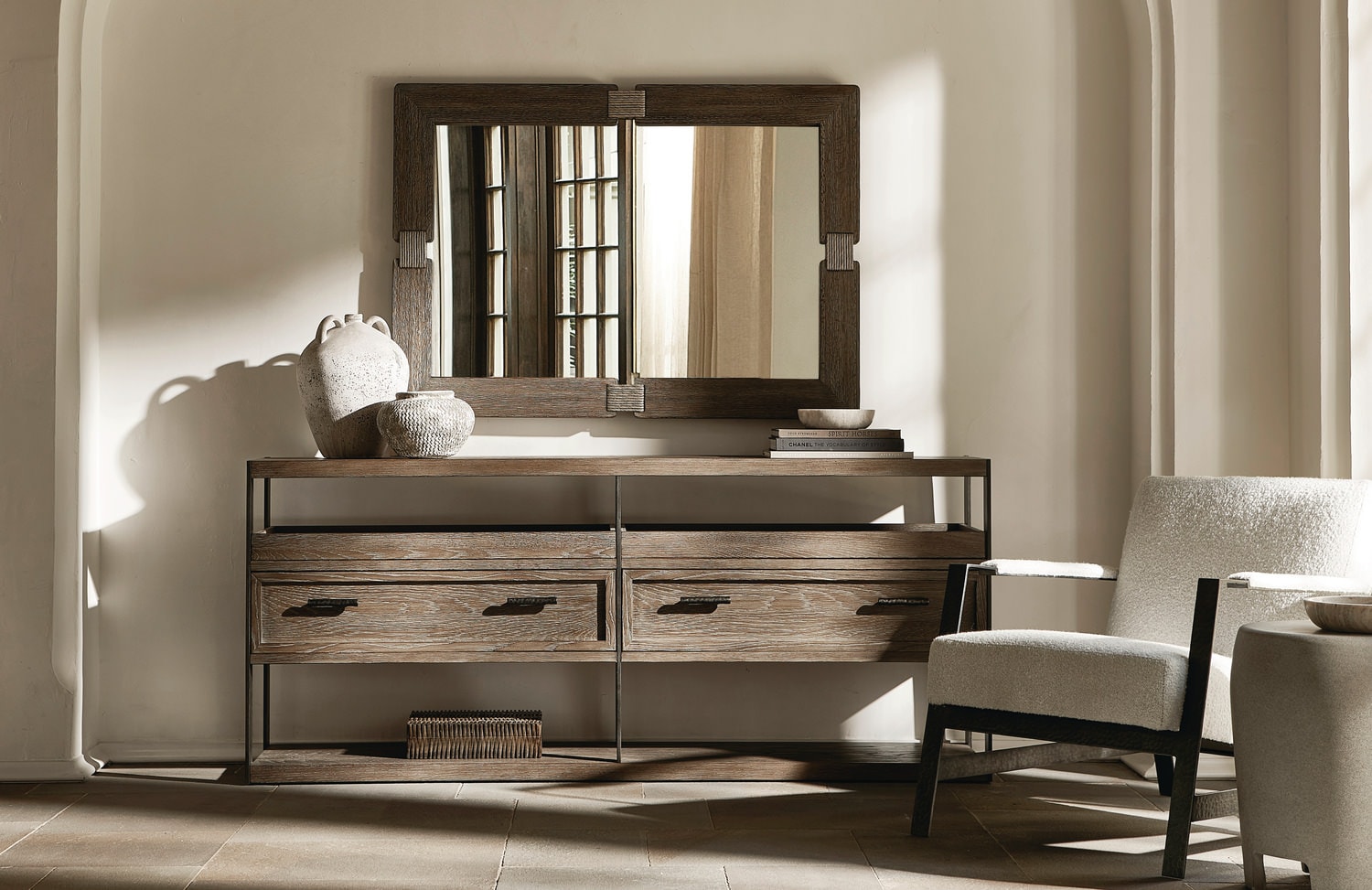 Elegant, sunlit bedroom featuring a large wooden dresser with a mirror and a comfortable chair
