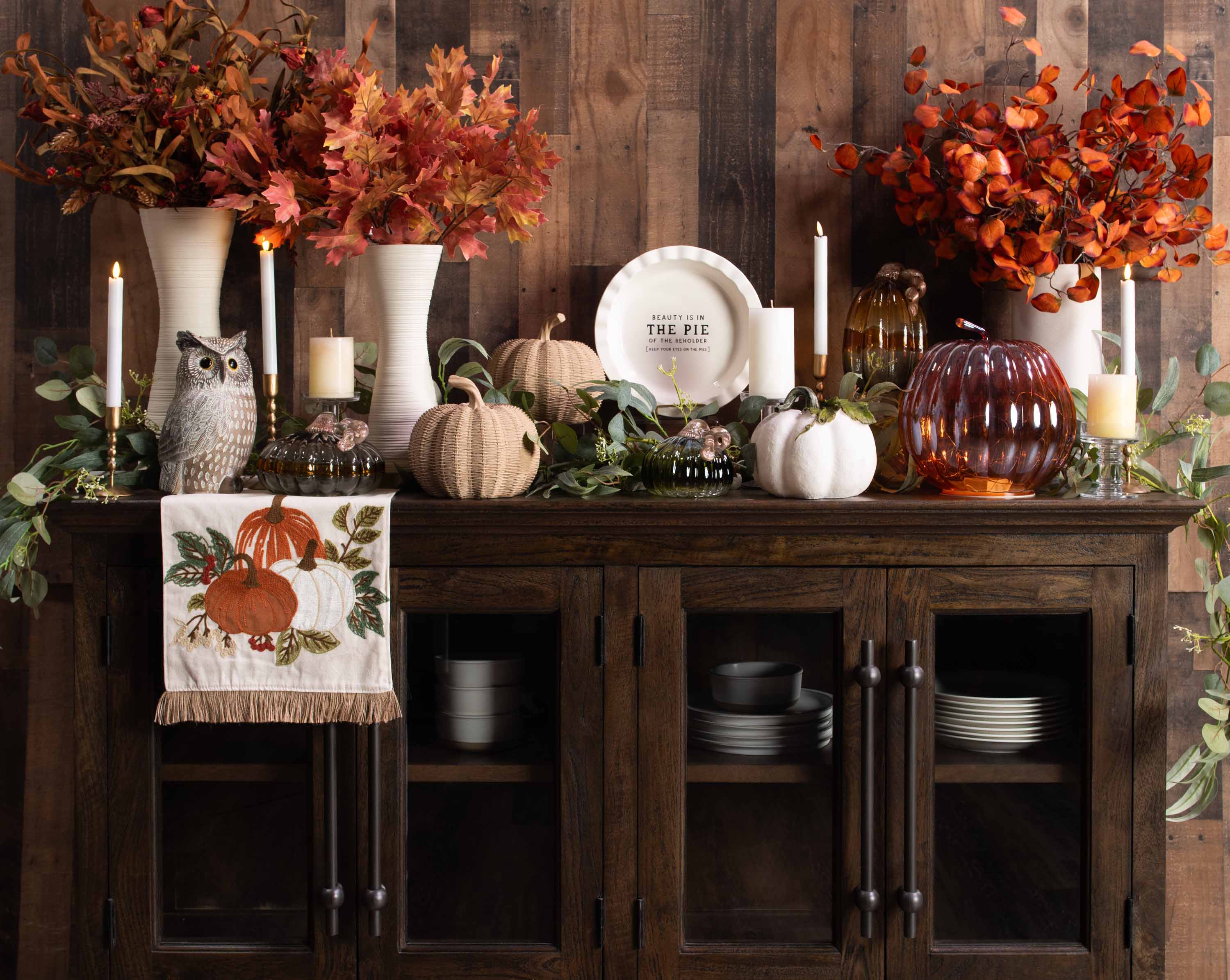 Rustic cabinet decorated with autumn-themed decor including pumpkins, candles, and fall foliage