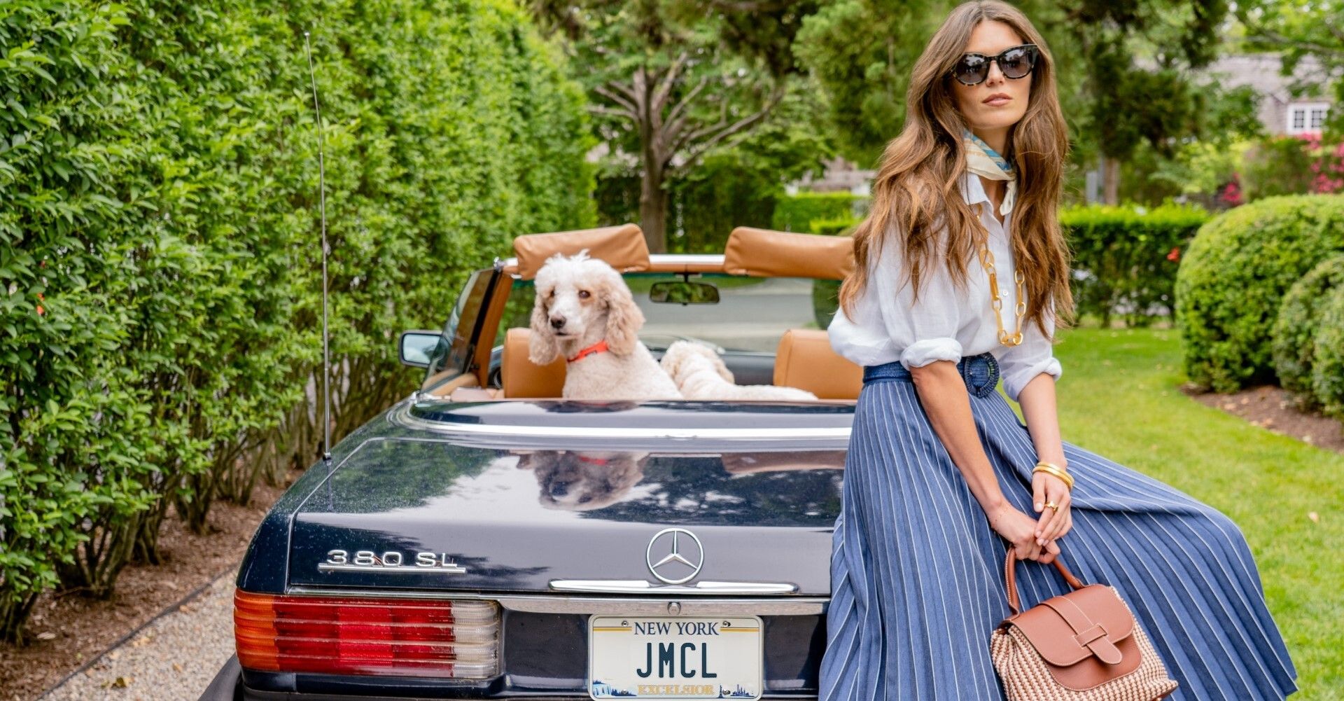 Woman and dog in convertible car, sunglasses, stylish outfits, greenery background