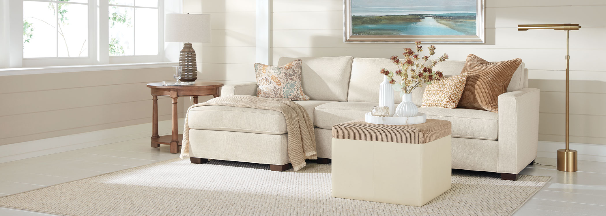 Modern living room with beige sofa, ottoman, side table, and floor lamp