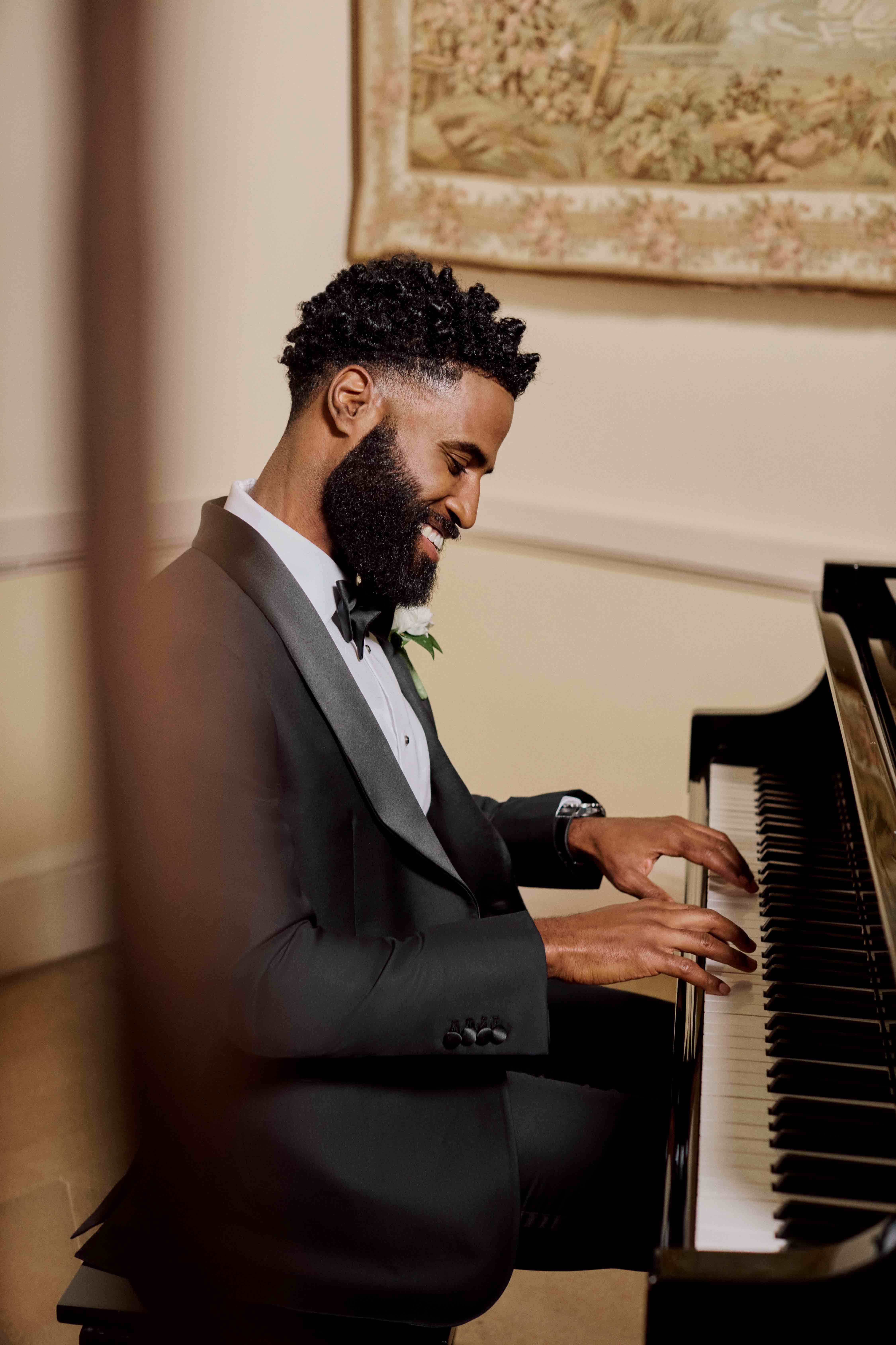 Man in a suit playing a grand piano, smiling gently