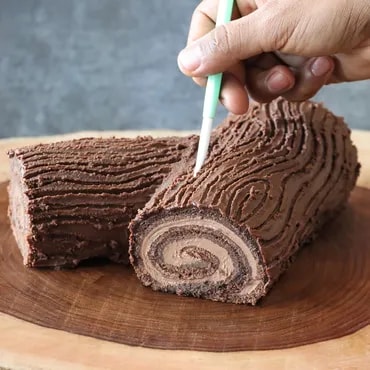 A hand cutting a slice from a chocolate yule log cake on a wooden board