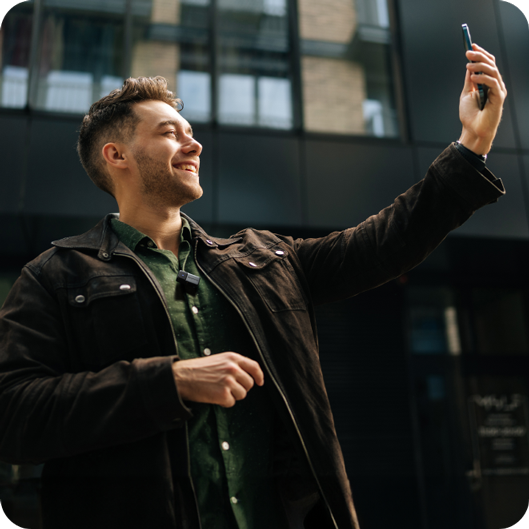 Smiling man in a jacket taking a selfie with his phone outdoors